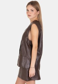 Gilet senza maniche in finta pelle marrone con vestibilità ampia, caratterizzato da ampie aperture per le braccia e un design elegante. Abbinato a una gonna coordinata.