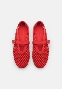 Chaussures tissées rouges avec un design texturé et ouvert, dotées d'une semelle plate et d'une bride réglable à la cheville. Fabriquées en matériau synthétique flexible.