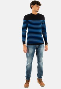 Maglione a righe blu e nere con scollatura a girocollo, realizzato in tessuto lavorato a maglia. Abbinato a jeans azzurri e stivali marroni con lacci.