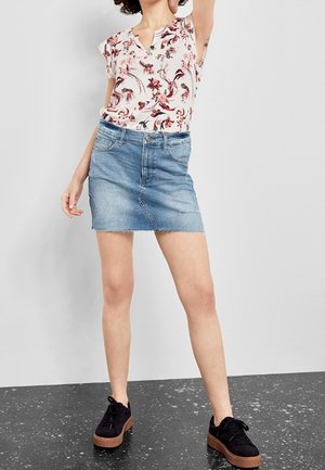 Blusa de estampado floral con mangas cortas, combinada con una minifalda vaquera azul claro. Zapatillas negras con suelas marrones completan el conjunto.