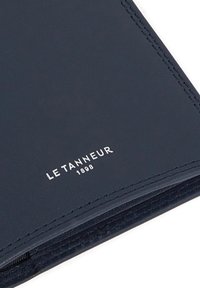 Cubierta de cuaderno de cuero marino con bordes cosidos y un logo plateado en relieve que dice "LE TANNEUR 1898." Textura suave, diseño minimalista.