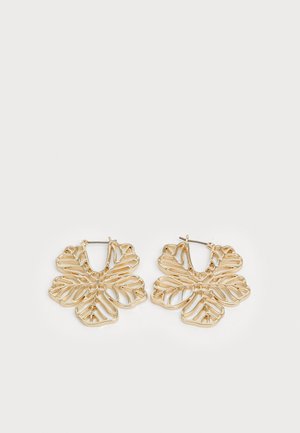 Brincos em metal dourado em forma de grandes folhas com recortes, apresentando um fecho de argola articulada e elementos de design orgânico.