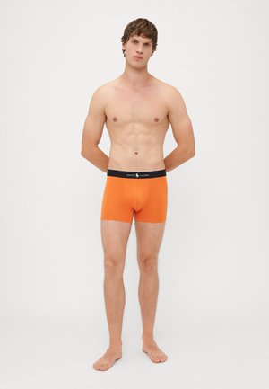 Oranžne bombažne bokserice z črnimi pasom, na katerem je logo Ralph Lauren. Prilegajo se tesno, tkanina pa ima gladko teksturo.