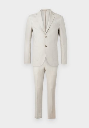 Costume beige clair en tissu à texture lisse. Veste avec revers cranté, deux boutons et trois poches. Pantalon ajusté.