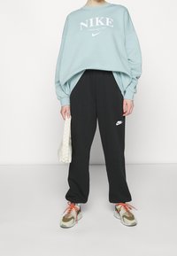 Světlounce modrá volná mikina s bílým logem Nike, černé kalhoty s bílým symbolem Nike swoosh a béžové tenisky s oranžovými tkaničkami.