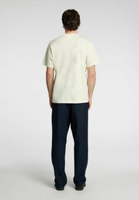 Lys gul kortærmet t-shirt med rund hals, parret med mørk marineblå brede bukser. Stoffet ser blødt og glat ud.