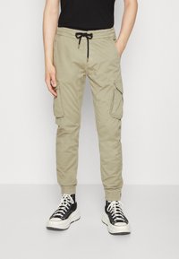 Khaki cargo-byxor med dragsko i midjan, smal passform, två sidofickor och två sidofickor. Bärs med svartvita sneakers.