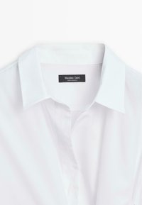 Chemise blanche à col classique pointu, partiellement boutonnée, étiquetée "Massimo Dutti" fabriquée au Maroc.