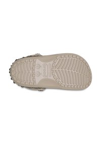 Schuhe mit einer strukturierten beigen Sohle, die erhabene kreisförmige und lineare Muster sowie metallische Nieten entlang der Kante aufweist. Crocs-Branding eingeprägt.