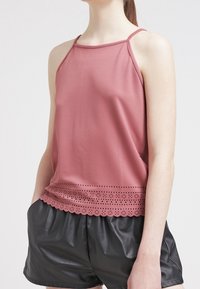 Top senza maniche in rosa polveroso con orlo in pizzo a scallop e dettagli perforati. Tessuto leggero con una vestibilità morbida, abbinato a pantaloni neri.