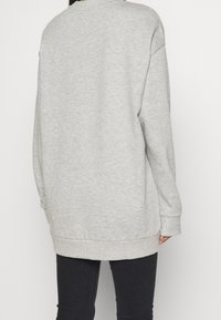 Felpa grigia oversize con collo rotondo, spalle scese e maniche lunghe. Texture morbida con orlo e polsini a coste.