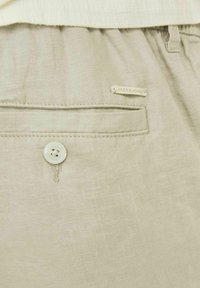 Svijetlosmeđi šortsevi od lana, s stražnjim džepom s bijelim dugmetom i malom oznakom s imenom branda "JACK & JONES."