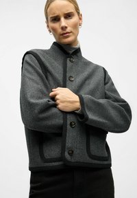 Gray wool jacket with a high collar, black trim, and large buttons. Features a cropped design and flap pockets on the front.