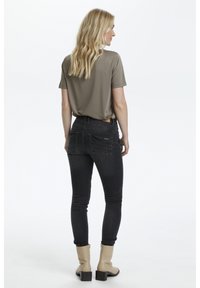Haut gris à manches courtes, jean skinny noir avec poches arrière, et bottines à talons blocs beige. Texture lisse et design ajusté.