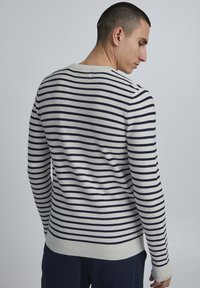 Pull rayé en bleu marine et crème. Présente des poignets et un ourlet côtelés, un col rond et un tissu texturé au dos.