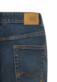 Jean en denim bleu foncé avec une étiquette en cuir beige comportant "camel active." Couture visible et détail de la poche arrière. Design décontracté.