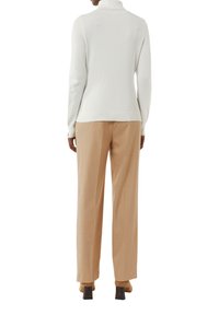 Maglione bianco a collo alto in tessuto morbido con dettagli a coste, abbinato a pantaloni beige su misura e scarpe con tacco marroni.