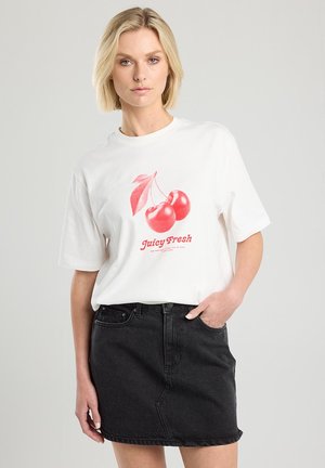 White cotton T-shirt featuring a graphic of red cherries and “Juicy Fresh” text below. Worn with a black denim skirt.