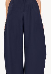 Pantalon large bleu marine en tissu lisse, doté de poches latérales et d'une taille haute pour une silhouette structurée.