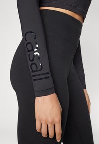 Black athletic leggings with shiny black “Casall” logo along the side, featuring a smooth texture and a fitted design.
