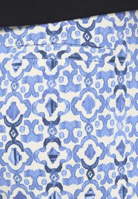 Patrón de tela floral geométrica en azul y blanco con una costura horizontal que atraviesa el centro.