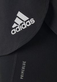 Černé sportovní oblečení s logem Adidas ve stříbrné barvě, vyrobené z materiálu Primeblue, s plochými švy a detaily na štítku.