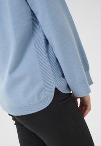 Maglione lavorato a maglia azzurro chiaro con polsini e orlo a costine, caratterizzato da una vestibilità comoda e spacchi laterali, abbinato a pantaloni neri aderenti.