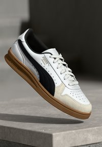 Sneaker bianco e blu navy caratterizzato da pelle liscia e camoscio, punta perforata, lacci piatti e suola in gomma. Contrassegnato da un logo.