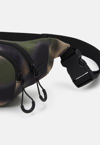 Riñonera de camuflaje con compartimentos con cremallera, fabricada en un tejido duradero, con herrajes negros y correa ajustable para un uso seguro.