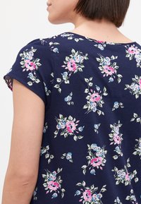 Camiseta de manga corta en azul marino con estampado floral, que presenta flores en tonos rosa, azul y verde sobre un tejido texturizado. Cuello redondo, diseño informal.