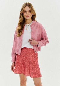 Różowa bomberka z oczkami, biała koszula i czerwona spódnica w kwiaty. Krótkie rękawy, lekki materiał i marszczony dół spódnicy.