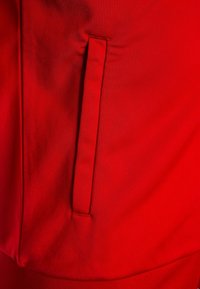 Červená sportovní tkanina s boční kapsou, která má čisté švy a hladkou texturu, poskytující elegantní vzhled a funkční design.