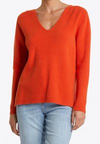 Pull orange à col en V, en tricot côtelé avec manches longues et coupe décontractée, fabriqué en tissu tricoté texturé. Associé à un jean bleu clair.