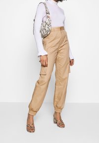 Beiga cargobyxor med elastiska muddar som har sidofickor. Bärs med en vit tight turtleneck och klacksandaler med ormskinnsmönster.