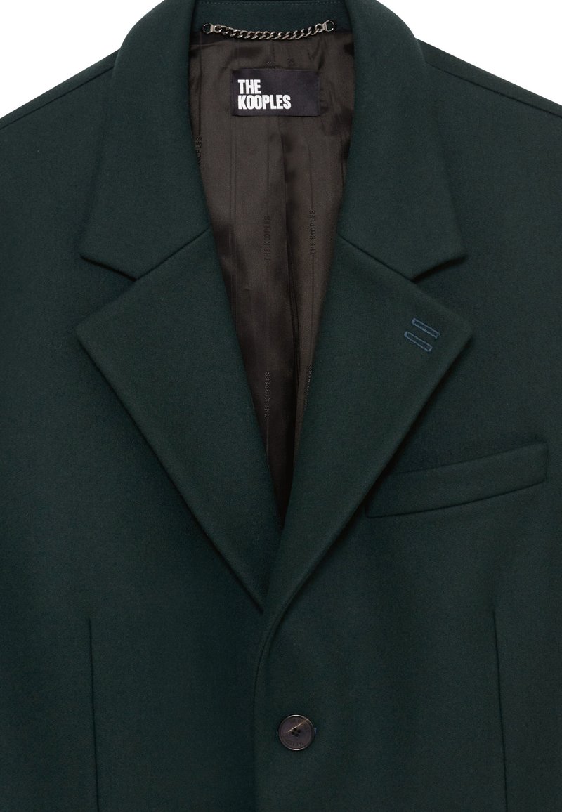 Dark green wool blazer with a notched collar, single button closure, and a sleek black satin lining. Features a chest pocket and decorative stitching.