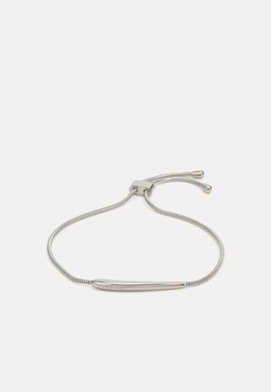 Bracelet en argent avec une barre en métal lisse et une chaîne ajustable, présentant une texture lisse et polie ainsi qu'un design minimaliste.