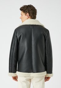 Giacca in pelle nera con un morbido collo e polsini in shearling di colore crema, presenta una cucitura posteriore e una finitura testurizzata.