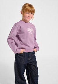 Lavendelkleurige sweatshirt met een centraal grafisch logo, ronde halslijn, geribbelde manchetten en zoom, gecombineerd met donkerblauwe spijkerbroeken.