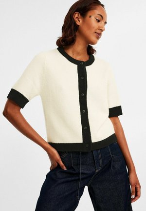 Kortærmet cardigan i creme med sorte kanter, med rund hals, fem knapper og en blød tekstur.