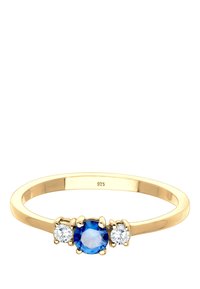 Anillo de plata chapado en oro con una piedra preciosa azul central, flanqueada por dos piedras transparentes, y una banda suave y redondeada. Marcado "925."