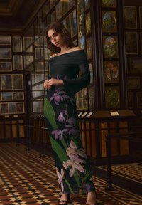 Sort off-the-shoulder kjole med blomsterdesign i lilla og grøn, med en tætsiddende silhuet og semi-gennemsigtige lange ærmer.