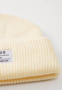 Berretto in maglia a coste giallo con risvolto e una piccola etichetta bianca con testo nero. Texture morbida, progettato per calore e comfort.