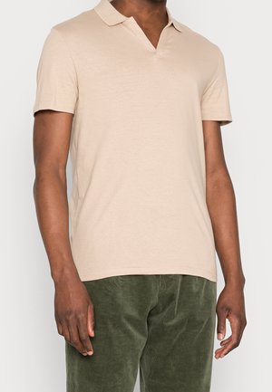 Beiges Kurzarm-Poloshirt mit V-Ausschnitt aus weichem Stoff, kombiniert mit grünen Cordhose.