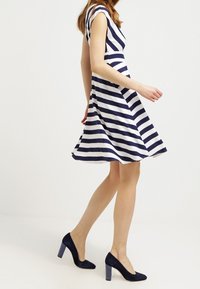 Marinblå och vit randig klänning med korta ärmar, utsvängd kjol och rund halsringning. Matchad med mörkblå mocka högklackade skor.