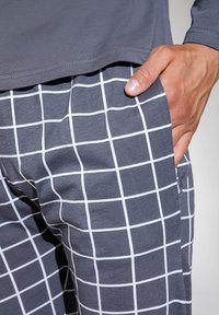 Szare bawełniane spodnie w białą kratę, zestawione z jednolitym szarym topem. Tkanina wydaje się miękka, a krój jest luźny.