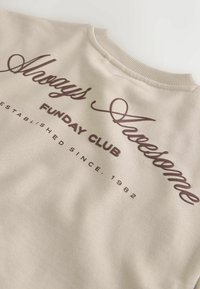 Beige sweatshirt with brown text reading Always Awesome, Funday Club, Established since 1982, folded to show collar and print details.