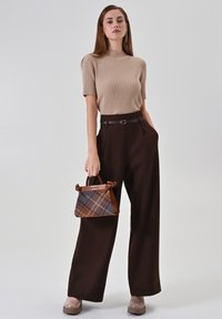 Beiges, geripptes Kurzarmtop, hoch taillierte braune Hose mit weitem Bein und eine braune karierte Handtasche mit strukturiertem Design. Braune Plateau-Schuhe.