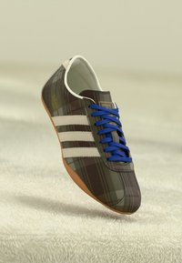 Sneaker a quadri marroni con tre strisce bianche. Lacci blu e suola in gomma marrone. Parte superiore in tessuto morbido e design a punta rotonda.