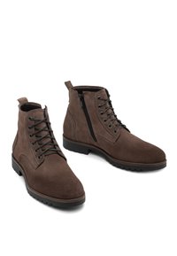 Bruine suède enkboots met veters en een zijrits. Heeft een gestructureerd oppervlak, ronde neus en rubberen loopzool voor grip.