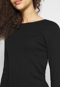 Schwarzes, geripptes Langarmshirt mit Rundhalsausschnitt, das eine weiche Stoffstruktur und eine taillierte Passform aufweist. Sichtbare Nahtdetails entlang der Nähte.